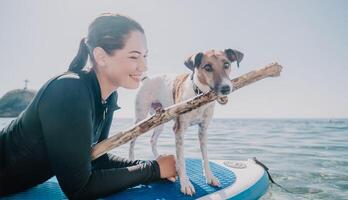 Sea woman sup. Silhouette of happy positive young woman with her dog, surfing on SUP board through calm water surface. Idyllic sunset. Active lifestyle at sea or river. Summer vacation with pets. photo