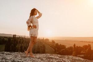 contento mujer en blanco boho vestir en puesta de sol en montañas. romántico mujer con largo pelo en pie con su espalda en el puesta de sol en naturaleza en verano con abierto manos. silueta. naturaleza. puesta de sol. foto