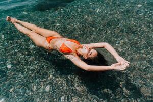 mujer nadando flotante en calma mar. contento sonriente mujer con largo pelo y ajuste cuerpo disfruta mar playa durante verano vacaciones vacaciones. concepto de cuerpo imagen y aptitud física, disfrutando un sereno playa. foto