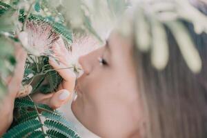 Beauty portrait of happy woman closeup. Young girl smelling Chinese acacia pink blossoming flowers. Portrait of young woman in blooming spring, summer garden. Romantic vibe. Female and nature photo