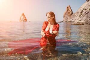 Woman travel sea. Happy tourist in red dress enjoy taking picture outdoors for memories. Woman traveler posing in sea beach, surrounded by volcanic mountains, sharing travel adventure journey photo