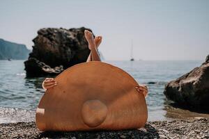 mujer viaje mar. contento turista en sombrero disfrutar tomando imagen al aire libre para recuerdos. mujer viajero posando en el playa a mar rodeado por volcánico montañas, compartiendo viaje aventuras viaje foto