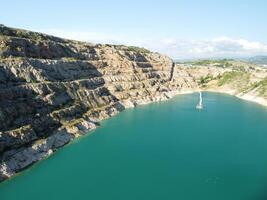 Aerial top view on opencast mining quarry with flooded bottom, turquoise surface of the lake. Quarry pond overgrown with green plants and clear turquoise water photo