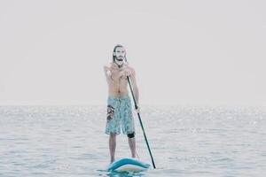 Man Sup Sea. Strong athletic man learns to paddle sup standing on board in open sea ocean on sunny day. Summer holiday vacation and travel concept. Aerial view. Slow motion photo