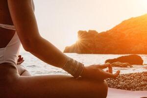 Woman sea yoga. Happy woman in white swimsuit and boho style braclets practicing outdoors on yoga mat by sea on sunset. Women yoga fitness routine. Healthy lifestyle, harmony and meditation photo