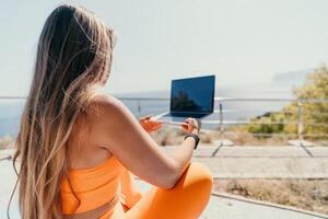 Woman laptop sea. Working remotely on seashore. Happy successful woman female freelancer working on laptop by the sea at sunset, makes a business transaction online. Freelance, remote work on vacation photo