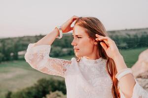 contento mujer en blanco boho vestir en puesta de sol en montañas. romántico mujer con largo pelo en pie con su espalda en el puesta de sol en naturaleza en verano con abierto manos. silueta. naturaleza. puesta de sol. foto