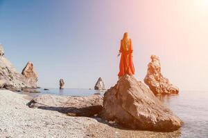 Woman travel sea. Young Happy woman in a long red dress posing on a beach near the sea on background of volcanic rocks, like in Iceland, sharing travel adventure journey photo