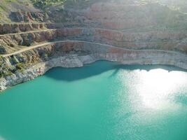 Aerial top view on opencast mining quarry with flooded bottom, turquoise surface of the lake. Quarry pond overgrown with green plants and clear turquoise water photo