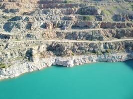 aéreo parte superior ver en a cielo abierto minería cantera con inundado abajo, turquesa superficie de el lago. cantera estanque descuidado con verde plantas y claro turquesa agua foto