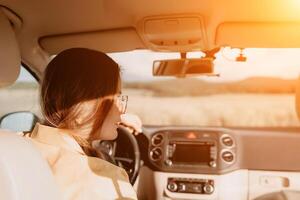 A woman in a yellow shirt is driving a car. She is wearing glasses and has her hands on the steering wheel photo