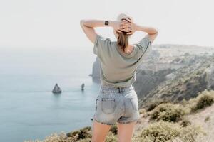 Woman travel sea. Happy tourist in hat enjoy taking picture outdoors for memories. Woman traveler posing on the beach at sea surrounded by volcanic mountains, sharing travel adventure journey photo