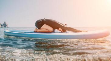 Woman sup yoga. Happy sporty woman practising yoga pilates on paddle sup surfboard. Female stretching doing workout on sea water. Modern individual female hipster outdoor summer sport activity. photo