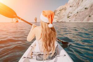 mujer en kayac espalda vista. contento joven mujer en Papa Noel sombrero flotante en kayac en calma mar. verano fiesta vacaciones y alegre hembra personas relajante teniendo divertido en el bote. foto