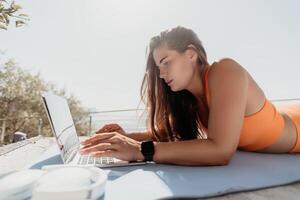 Woman laptop sea. Working remotely on seashore. Happy successful woman female freelancer working on laptop by the sea at sunset, makes a business transaction online. Freelance, remote work on vacation photo