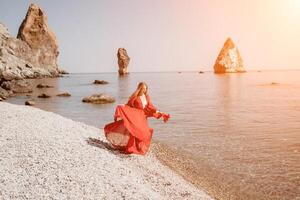 mujer viaje mar. contento turista en rojo vestir disfrutar tomando imagen al aire libre para recuerdos. mujer viajero posando en el rock a mar bahía rodeado por volcánico montañas, compartiendo viaje aventuras viaje foto