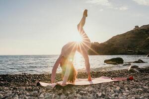 Woman sea yoga. Happy woman with black hair doing Pilates with the ring on the yoga mat near the sea on the pebble beach. Female fitness yoga concept. Healthy lifestyle, harmony and meditation. photo