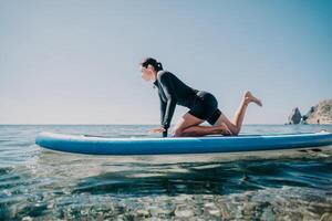 Woman sup yoga. Happy sporty woman practising yoga pilates on paddle sup surfboard. Female stretching doing workout on sea water. Modern individual female hipster outdoor summer sport activity. photo