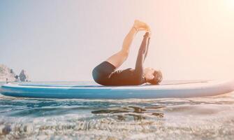 Woman sup yoga. Happy sporty woman practising yoga pilates on paddle sup surfboard. Female stretching doing workout on sea water. Modern individual female hipster outdoor summer sport activity. photo