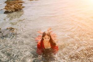 Woman travel sea. Happy tourist in red dress enjoy taking picture outdoors for memories. Woman traveler posing in sea beach, surrounded by volcanic mountains, sharing travel adventure journey photo