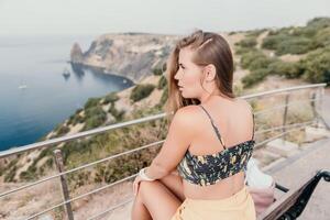 Woman travel sea. Happy tourist enjoy taking picture outdoors for memories. Woman traveler looks at the edge of the cliff on the sea bay of mountains, sharing travel adventure journey photo