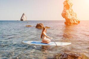 Woman sea sup. Close up portrait of happy young caucasian woman with long hair looking at camera and smiling. Cute woman portrait in a blue bikini posing on sup board in the sea photo