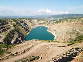 Aerial top view on opencast mining quarry with flooded bottom, turquoise surface of the lake. Quarry pond overgrown with green plants and clear turquoise water photo