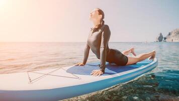 Woman sup yoga. Happy sporty woman practising yoga pilates on paddle sup surfboard. Female stretching doing workout on sea water. Modern individual female hipster outdoor summer sport activity. photo