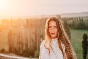 Happy woman in white boho dress on sunset in mountains. Romantic woman with long hair standing with her back on the sunset in nature in summer with open hands. Silhouette. Nature. Sunset. photo