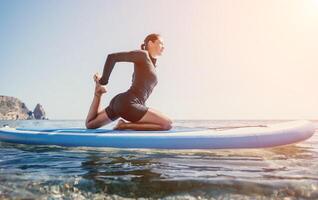 Woman sup yoga. Happy sporty woman practising yoga pilates on paddle sup surfboard. Female stretching doing workout on sea water. Modern individual female hipster outdoor summer sport activity. photo