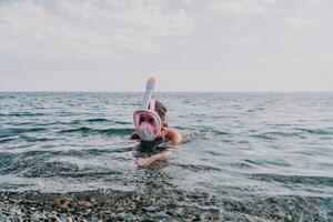 Young happy woman in white bikini and wearing pink mask gets ready for sea snorkeling. Positive smiling woman relaxing and enjoying water activities with family summer travel holidays vacation on sea. photo