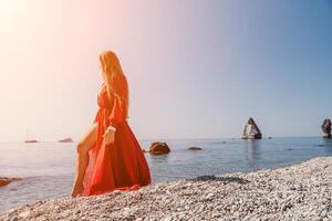 Woman travel sea. Happy tourist in red dress enjoy taking picture outdoors for memories. Woman traveler posing on the rock at sea bay surrounded by volcanic mountains, sharing travel adventure journey photo