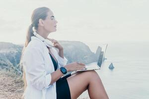 Woman sea laptop. Business woman, freelancer with laptop working over blue sea beach. Happy smiling girl relieves stress from work. Freelance, remote work on vacation, digital nomad, travel concept photo