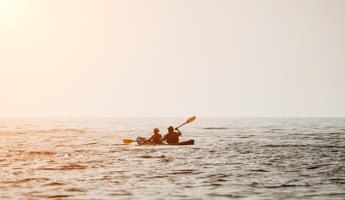 Happy couple kayaks in an inflatable kayak on the sea at sunset. Couple kanoeing in the sea near the island with mountains. People kayaking in life jackets sail. Back view photo