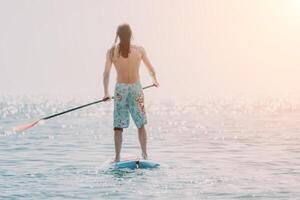 Man Sup Sea. Strong athletic man learns to paddle sup standing on board in open sea ocean on sunny day. Summer holiday vacation and travel concept. Aerial view. Slow motion photo