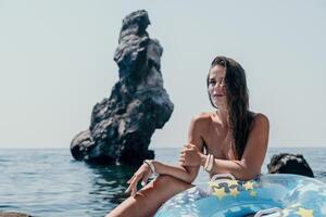 mujer verano mar. contento mujer nadando con inflable rosquilla en el playa en verano soleado día, rodeado por volcánico montañas. verano vacaciones concepto. foto