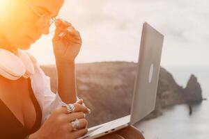 Woman sea laptop. Business woman, freelancer with laptop working over blue sea beach. Happy smiling girl relieves stress from work. Freelance, remote work on vacation, digital nomad, travel concept photo