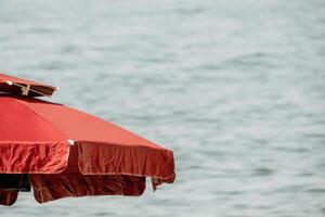 Red Beach Umbrella on the Background of the Blue Sea Ocean. Beach Landscape. Summer travel and holidays concept. photo