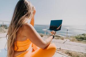 Woman laptop sea. Working remotely on seashore. Happy successful woman female freelancer working on laptop by the sea at sunset, makes a business transaction online. Freelance, remote work on vacation photo