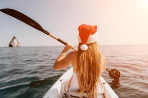 mujer en kayac espalda vista. contento joven mujer en Papa Noel sombrero flotante en kayac en calma mar. verano fiesta vacaciones y alegre hembra personas relajante teniendo divertido en el bote. foto