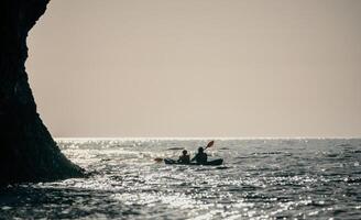 contento Pareja kayaks en un inflable kayac en el mar a puesta de sol. Pareja piragüismo en el mar cerca el isla con montañas. personas kayak en vida chaquetas navegar. espalda ver foto