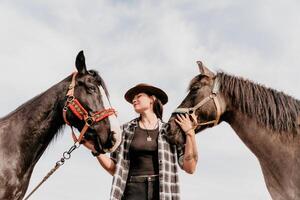 Young happy woman in hat with her horse in evening sunset light. Outdoor photography with fashion model girl. Lifestyle mood. Concept of outdoor riding, sports and recreation. photo