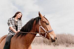 Young happy woman in hat with her horse in evening sunset light. Outdoor photography with fashion model girl. Lifestyle mood. Concept of outdoor riding, sports and recreation. photo