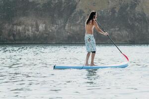 Man Sup Sea. Strong athletic man learns to paddle sup standing on board in open sea ocean on sunny day. Summer holiday vacation and travel concept. Aerial view. Slow motion photo