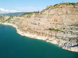 Aerial top view on opencast mining quarry with flooded bottom, turquoise surface of the lake. Quarry pond overgrown with green plants and clear turquoise water photo