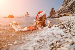 Woman travel sea. Happy tourist enjoy taking picture on the beach for memories. Woman traveler in Santa hat looks at camera on the sea bay, sharing travel adventure journey photo