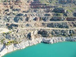 Aerial top view on opencast mining quarry with flooded bottom, turquoise surface of the lake. Quarry pond overgrown with green plants and clear turquoise water photo