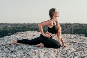 Fitness woman. Well looking middle aged woman with long hair, fitness instructor in leggings and tops doing stretching and pilates on the rock near forest. Female fitness yoga routine concept. photo