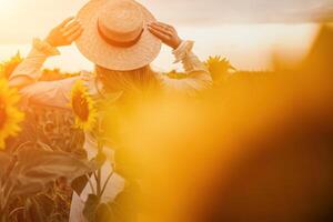 Woman in Sunflower Field. Happy girl in a straw hat posing in a vast field of sunflowers at sunset, enjoy taking picture outdoors for memories. Summer time. photo