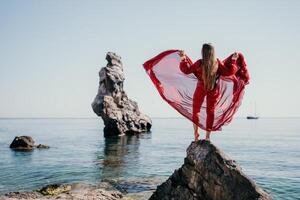 Woman travel sea. Young Happy woman in a long red dress posing on a beach near the sea on background of volcanic rocks, like in Iceland, sharing travel adventure journey photo